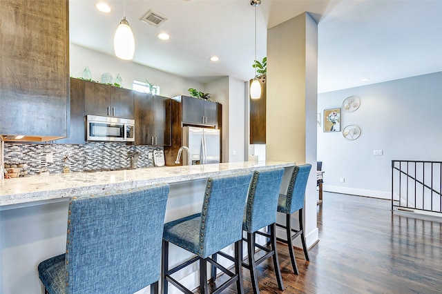 kitchen featuring a kitchen breakfast bar, decorative backsplash, dark brown cabinetry, kitchen peninsula, and stainless steel appliances