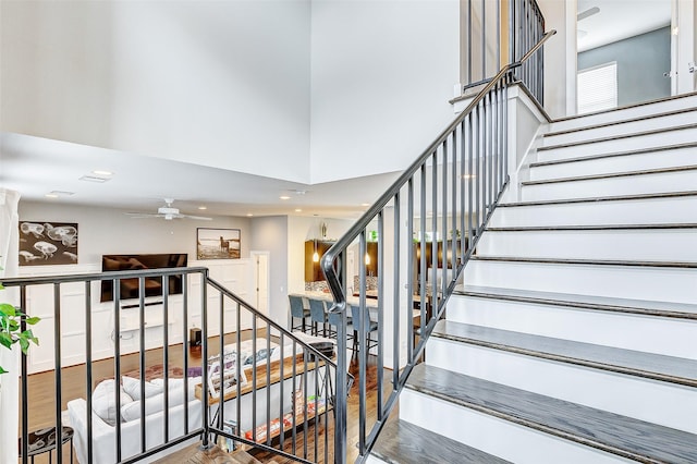 stairway featuring wood-type flooring, ceiling fan, and a high ceiling