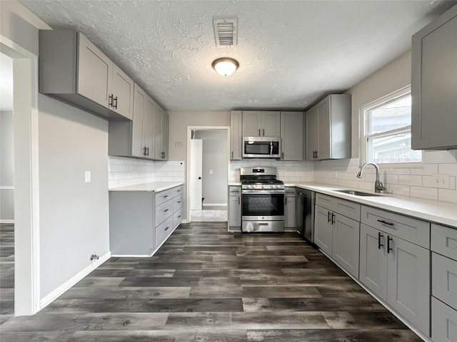 kitchen with dark hardwood / wood-style flooring, stainless steel appliances, tasteful backsplash, sink, and gray cabinetry