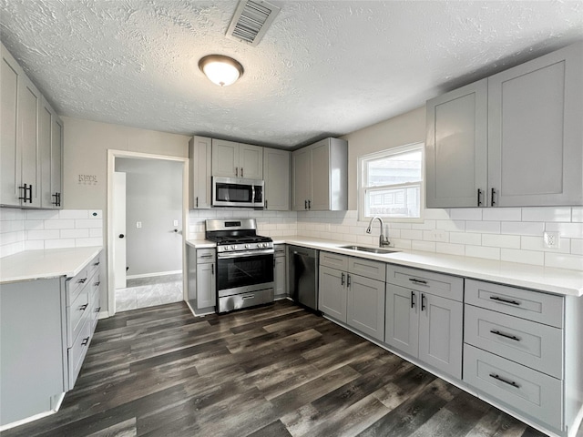 kitchen with gray cabinets, stainless steel appliances, backsplash, dark hardwood / wood-style flooring, and sink