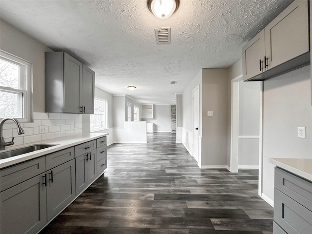 kitchen featuring a textured ceiling, dark wood-type flooring, decorative backsplash, sink, and gray cabinetry