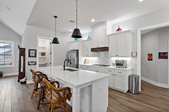 kitchen featuring a center island with sink, appliances with stainless steel finishes, decorative light fixtures, vaulted ceiling, and white cabinets