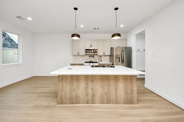 kitchen featuring backsplash, a center island with sink, sink, stainless steel appliances, and white cabinets