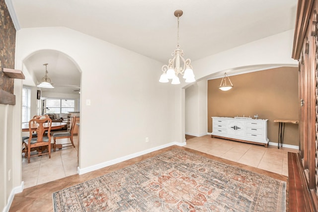 interior space featuring arched walkways, a notable chandelier, light tile patterned floors, vaulted ceiling, and baseboards