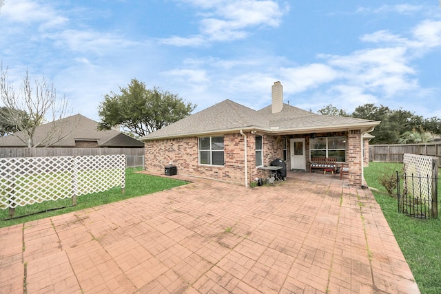 back of property featuring brick siding, a chimney, a shingled roof, a patio area, and a fenced backyard