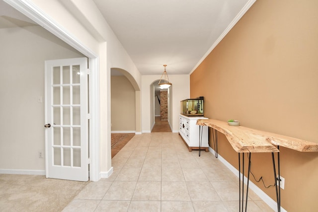 hall featuring light tile patterned floors, baseboards, arched walkways, and crown molding