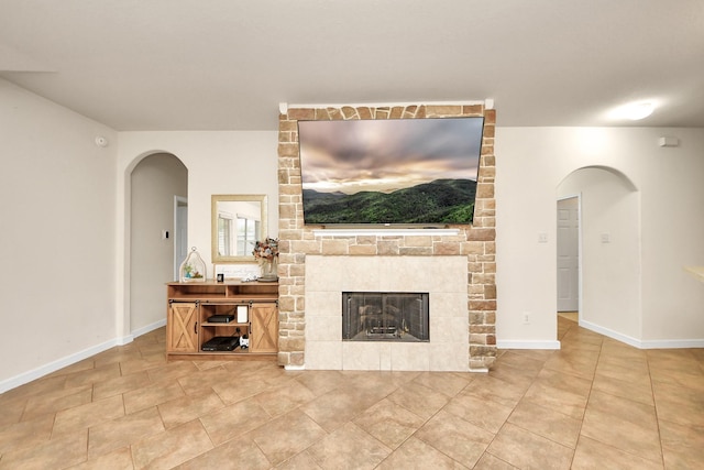 unfurnished living room with arched walkways, a fireplace, baseboards, and tile patterned floors