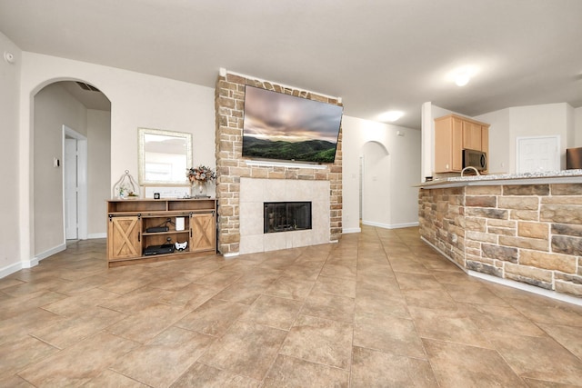 living area with arched walkways, a brick fireplace, and baseboards