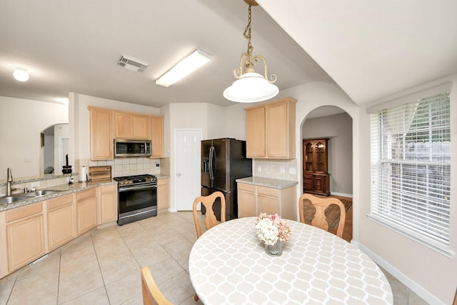 kitchen featuring arched walkways, decorative light fixtures, appliances with stainless steel finishes, light brown cabinets, and a sink