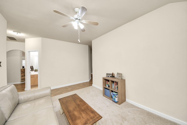 living room with visible vents, arched walkways, baseboards, light colored carpet, and ceiling fan