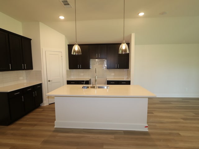kitchen featuring a kitchen island with sink, backsplash, visible vents, wood finished floors, and a sink