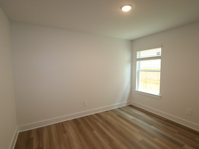unfurnished room with baseboards and dark wood-style floors