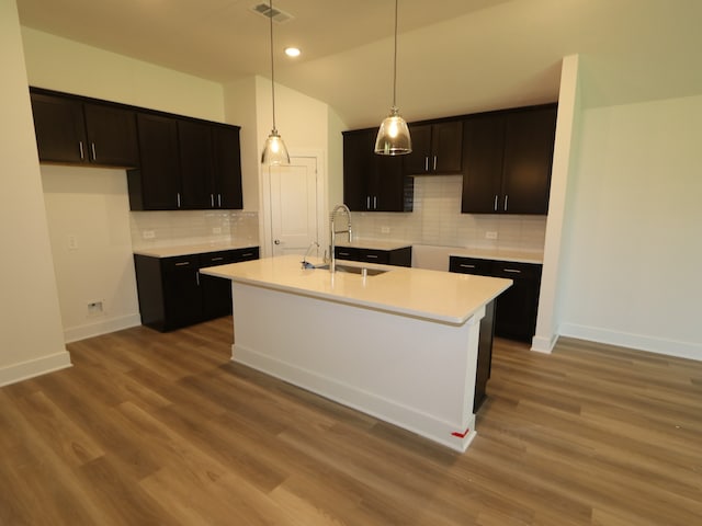 kitchen with backsplash, visible vents, a sink, baseboards, and an island with sink