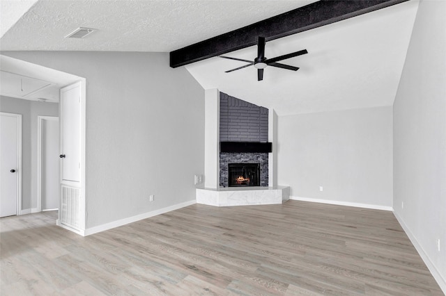 unfurnished living room with ceiling fan, light wood-type flooring, a fireplace, a textured ceiling, and lofted ceiling with beams