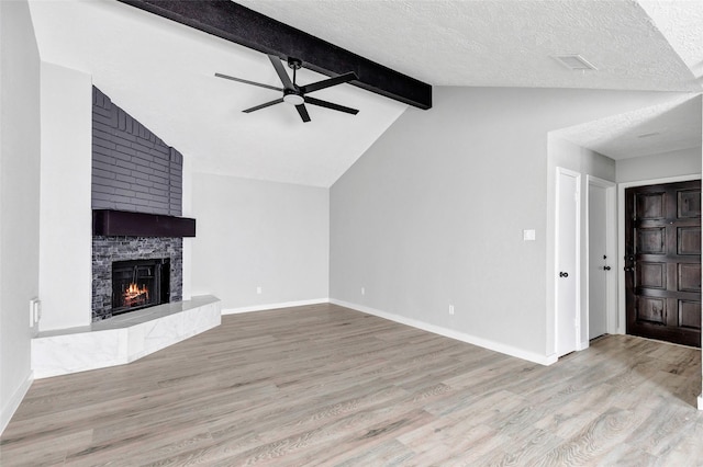 unfurnished living room with ceiling fan, lofted ceiling with beams, a large fireplace, light hardwood / wood-style flooring, and a textured ceiling