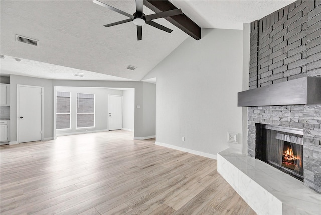 unfurnished living room with ceiling fan, a fireplace, light hardwood / wood-style floors, lofted ceiling with beams, and a textured ceiling