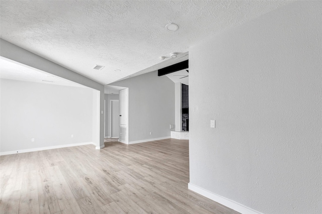 empty room featuring lofted ceiling, light wood-type flooring, a fireplace, and a textured ceiling