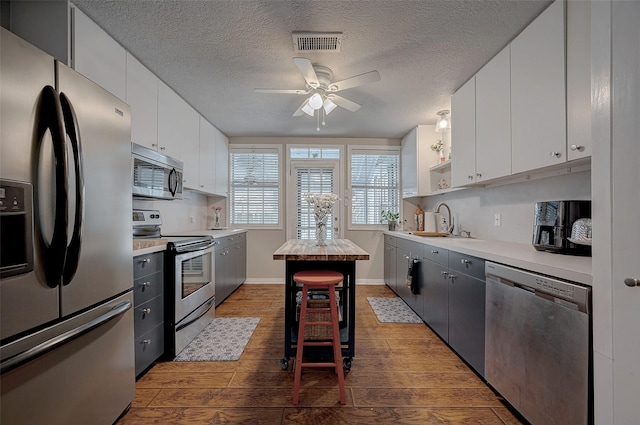 kitchen featuring sink, white cabinets, stainless steel appliances, dark wood-type flooring, and a textured ceiling