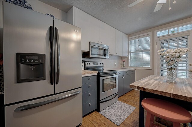 kitchen with gray cabinetry, a textured ceiling, stainless steel appliances, light hardwood / wood-style floors, and white cabinets