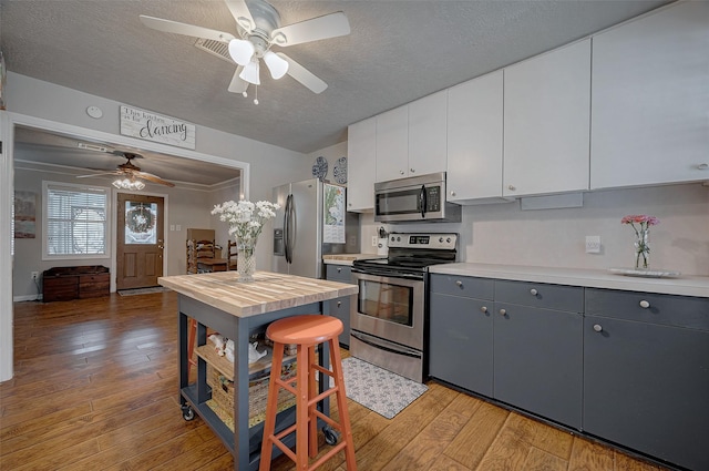 kitchen with gray cabinets, light hardwood / wood-style flooring, appliances with stainless steel finishes, white cabinetry, and a textured ceiling