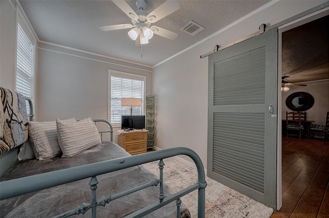 bedroom featuring dark wood-type flooring, ceiling fan, ornamental molding, a textured ceiling, and a barn door