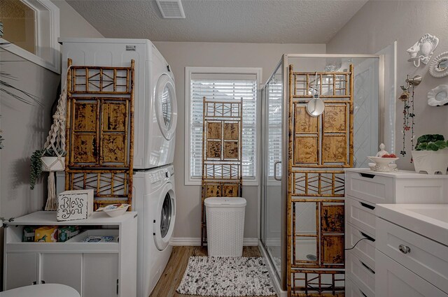 clothes washing area with stacked washer and clothes dryer, light hardwood / wood-style flooring, and a textured ceiling