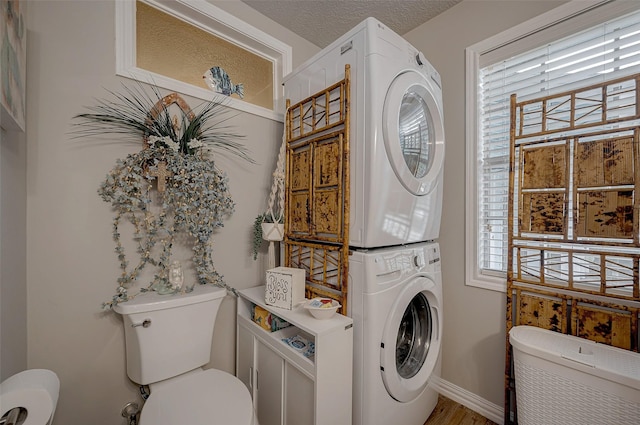 clothes washing area with stacked washer and dryer, plenty of natural light, wood-type flooring, and a textured ceiling