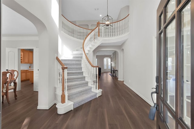 foyer with crown molding, a towering ceiling, dark hardwood / wood-style floors, and a notable chandelier