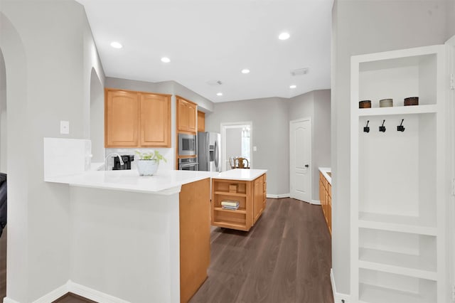 kitchen with built in features, kitchen peninsula, appliances with stainless steel finishes, and dark hardwood / wood-style floors