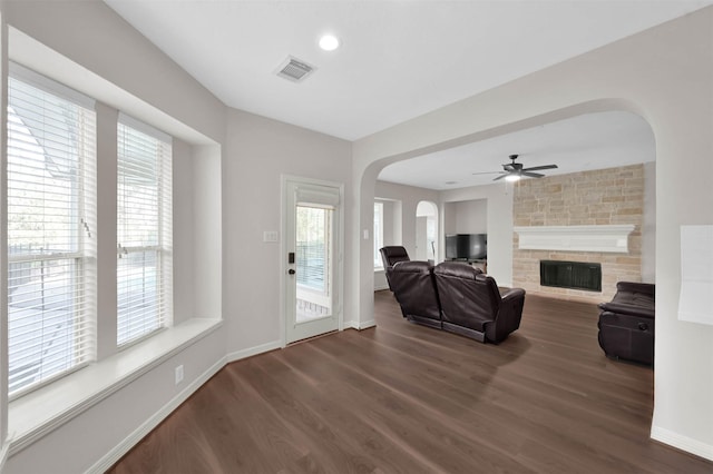 living room featuring ceiling fan, dark hardwood / wood-style floors, and a stone fireplace