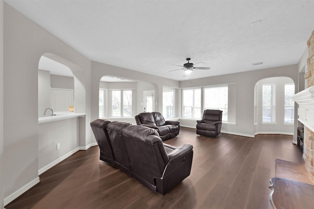 living room with ceiling fan, a large fireplace, and dark hardwood / wood-style floors