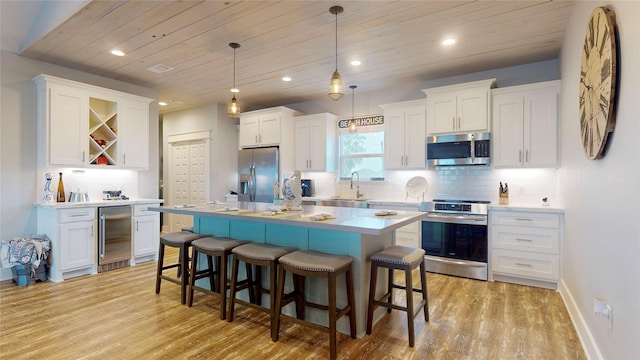 kitchen featuring white cabinets, beverage cooler, a center island, decorative light fixtures, and stainless steel appliances