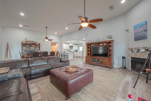 living room with a fireplace, vaulted ceiling, ceiling fan, and light wood-type flooring