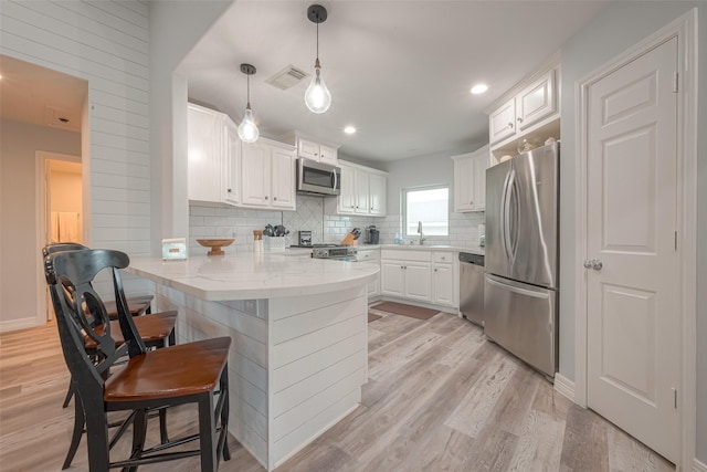 kitchen featuring kitchen peninsula, stainless steel appliances, pendant lighting, white cabinets, and sink