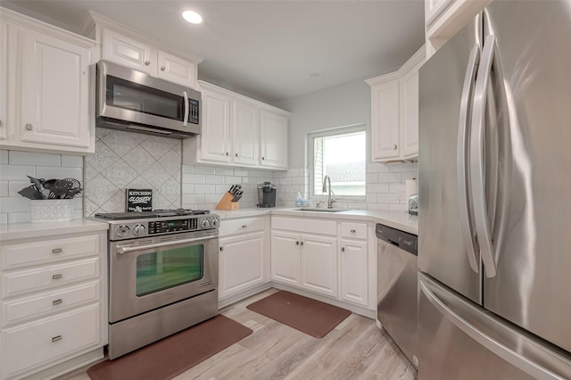 kitchen featuring tasteful backsplash, sink, white cabinetry, light hardwood / wood-style flooring, and stainless steel appliances