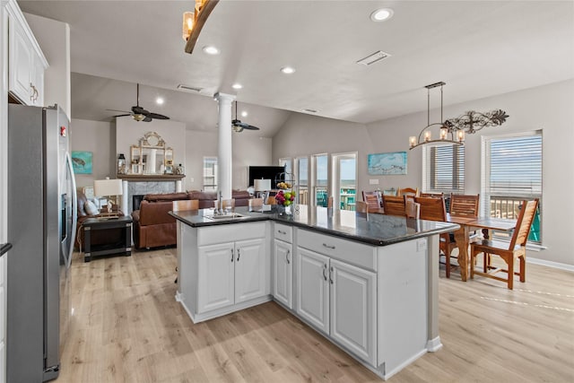 kitchen with a ceiling fan, white cabinets, open floor plan, stainless steel fridge, and decorative columns