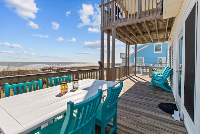 wooden deck with a water view, a beach view, and outdoor dining space