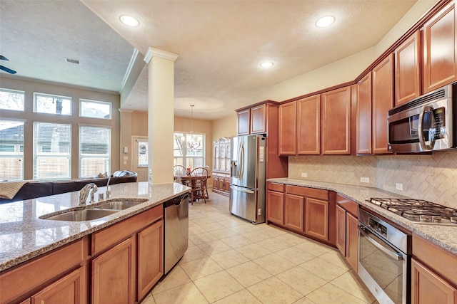 kitchen with light stone countertops, appliances with stainless steel finishes, decorative light fixtures, sink, and backsplash