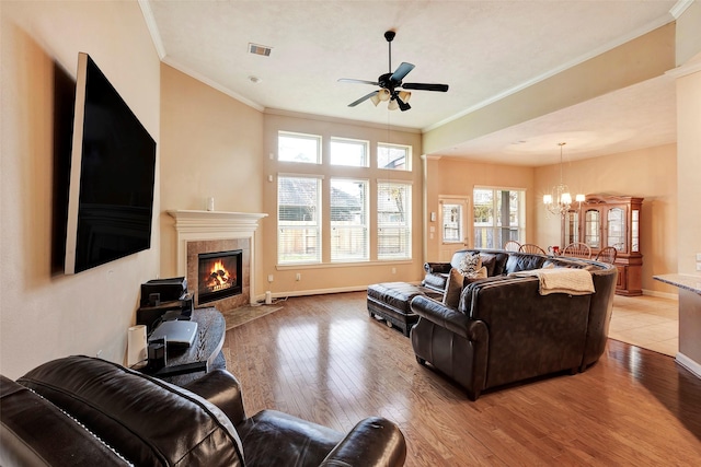 living room with ceiling fan with notable chandelier, a tile fireplace, light hardwood / wood-style flooring, and ornamental molding