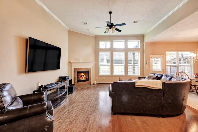 living room featuring light hardwood / wood-style floors, a tile fireplace, crown molding, and ceiling fan with notable chandelier