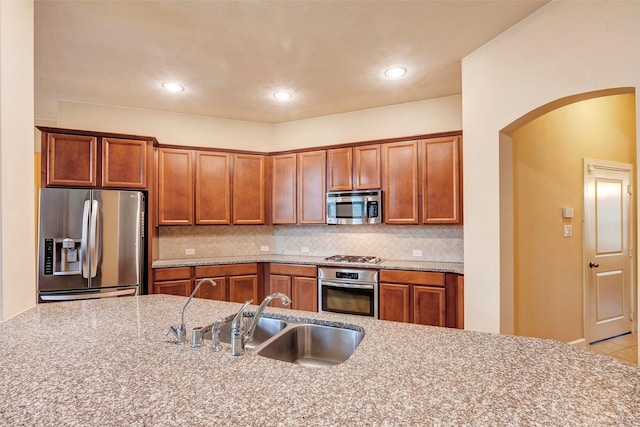 kitchen with light stone countertops, stainless steel appliances, decorative backsplash, and sink