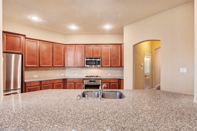 kitchen with tasteful backsplash, appliances with stainless steel finishes, sink, and light stone counters