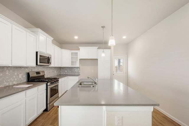 kitchen with sink, hanging light fixtures, appliances with stainless steel finishes, and a kitchen island with sink