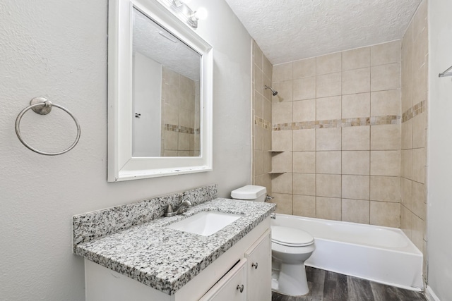 full bathroom with a textured ceiling, tiled shower / bath, wood-type flooring, vanity, and toilet