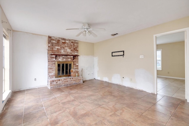 unfurnished living room featuring a brick fireplace, light tile patterned floors, and ceiling fan