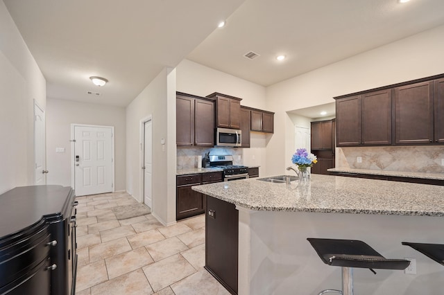 kitchen with light stone countertops, dark brown cabinetry, appliances with stainless steel finishes, decorative backsplash, and sink