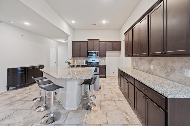 kitchen featuring light stone countertops, stainless steel appliances, tasteful backsplash, sink, and a center island with sink