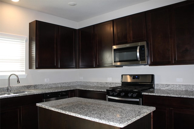 kitchen with stainless steel appliances, light stone countertops, sink, and dark brown cabinets