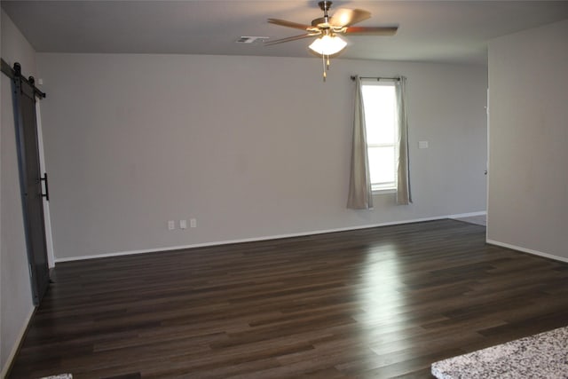 empty room featuring dark hardwood / wood-style floors, ceiling fan, and a barn door