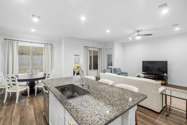 kitchen featuring light stone countertops, dark wood-type flooring, white cabinetry, sink, and a center island with sink